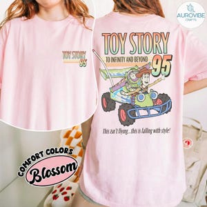 Pu&ograve; includere: T-shirt rosa chiaro con grafica "Toy Story 95" sul davanti e un disegno pi&ugrave; grande sul retro con Buzz Lightyear e Woody su un veicolo. Il disegno sul retro include il testo "TO INFINITY AND BEYOND" e "This isn't flying...this is falling with style!"