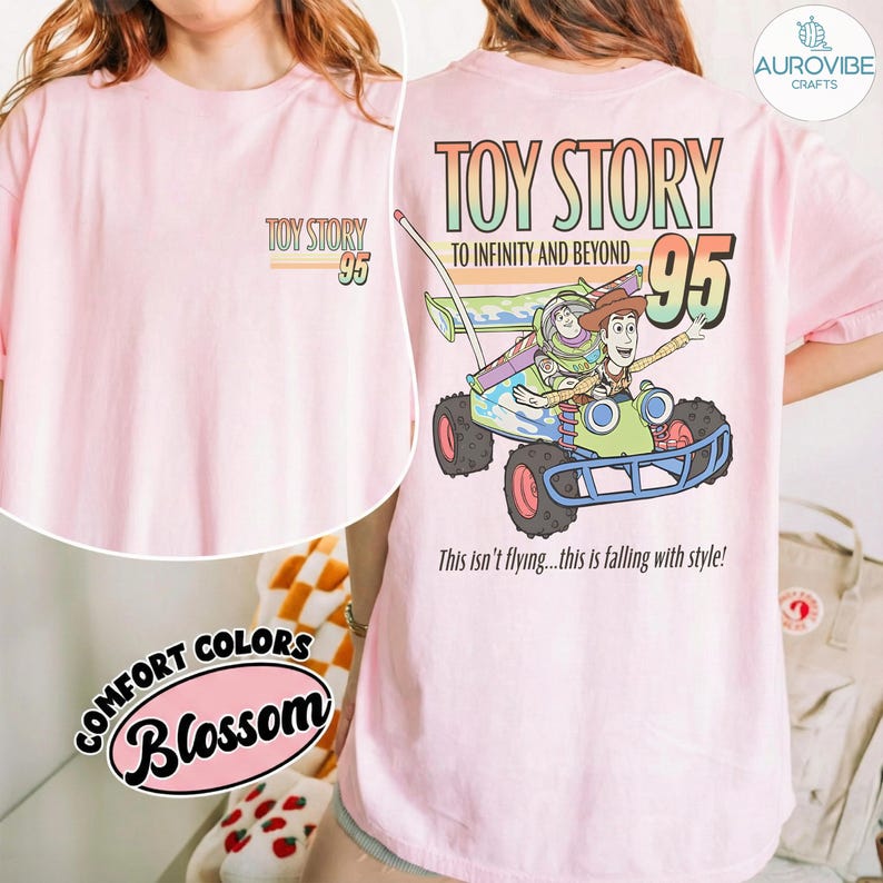 Pu&ograve; includere: T-shirt rosa chiaro con grafica "Toy Story 95" sul davanti e un disegno pi&ugrave; grande sul retro con Buzz Lightyear e Woody su un veicolo. Il disegno sul retro include il testo "TO INFINITY AND BEYOND" e "This isn't flying...this is falling with style!"