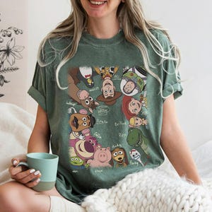 K&ouml;nnte beinhalten: Gr&uuml;nes T-Shirt mit einem farbenfrohen Aufdruck von Charakteren aus dem Animationsfilm Toy Story. Das Design zeigt Woody, Buzz Lightyear, Jessie und weitere Figuren. Das T-Shirt hat eine lockere Passform.