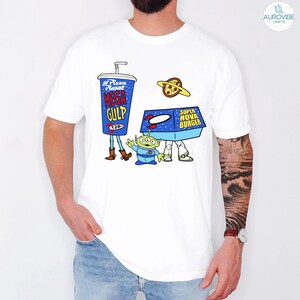 以下が含まれることがあります： 映画トイ・ストーリーのキャラクターが描かれた漫画デザインの白いTシャツ。デザインには、青いメガガルフカップ、緑色のエイリアン、スーパーノヴァバーガーボックス、ピザプラネットが含まれています。シャツはクルーネックで半袖です。