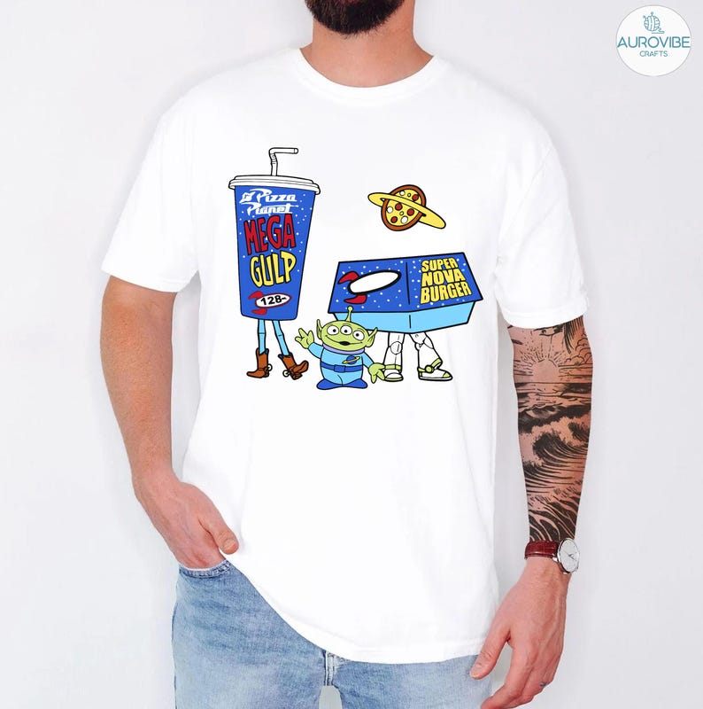以下が含まれることがあります： 映画トイ・ストーリーのキャラクターが描かれた漫画デザインの白いTシャツ。デザインには、青いメガガルフカップ、緑色のエイリアン、スーパーノヴァバーガーボックス、ピザプラネットが含まれています。シャツはクルーネックで半袖です。