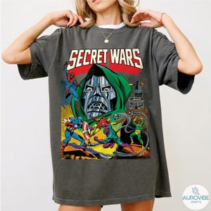 May include: Dark gray t-shirt featuring a comic book illustration with the text "SECRET WARS". The graphic includes characters like Spider-Man, Captain America, and Doctor Doom in a colorful action scene.