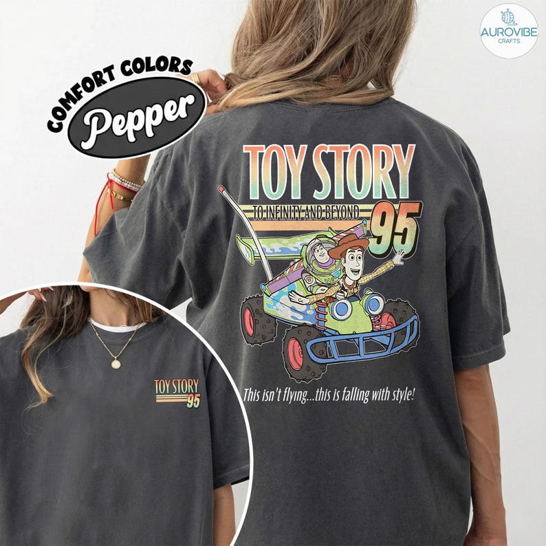 Pu&ograve; includere: T-shirt grigio scuro con una grafica colorata di Toy Story. Il design presenta Buzz Lightyear e Woody in un'auto da corsa, con il testo "TOY STORY 95" e "This isn't flying...this is falling with style!"