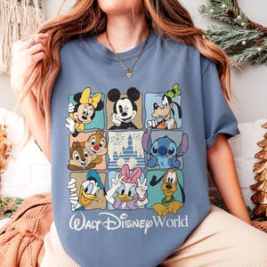 May include: A light blue t-shirt featuring a grid of Disney characters including Mickey Mouse, Minnie Mouse, Donald Duck, and Goofy. The words "Walt Disney World" are printed in white script below the grid.