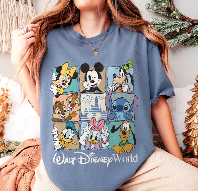 May include: A light blue t-shirt featuring a grid of Disney characters including Mickey Mouse, Minnie Mouse, Donald Duck, and Goofy. The words "Walt Disney World" are printed in white script below the grid.