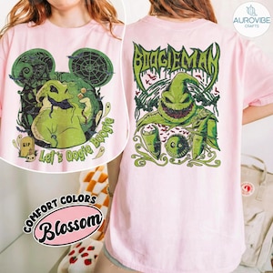 May include: A light pink t-shirt featuring a graphic of a green burlap sack character with a wide grin. The back design displays the text BOOGIEMAN in a stylised font above the character, while the front design shows the character with the text Let's Oogie Boogie and a tombstone marked RIP.