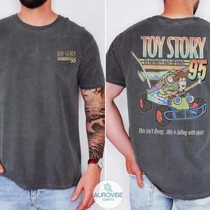 Pu&ograve; includere: T-shirt grigio scuro con la scritta "TOY STORY 95" sul davanti. Il retro presenta una grafica colorata di Buzz Lightyear e Woody in un'auto, con il testo "TO INFINITY AND BEYOND" e "This isn't flying... this is falling with style!"
