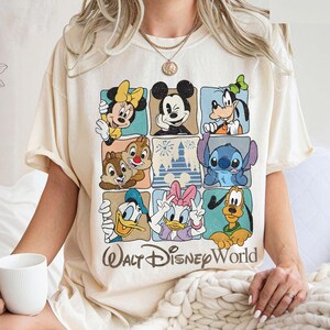 May include: Cream-colored t-shirt featuring a grid of Disney characters including Mickey Mouse, Minnie Mouse, Goofy, Donald Duck, Daisy Duck, Chip and Dale, Stitch, and Pluto. The words "Walt Disney World" are printed below the grid in a brown font.