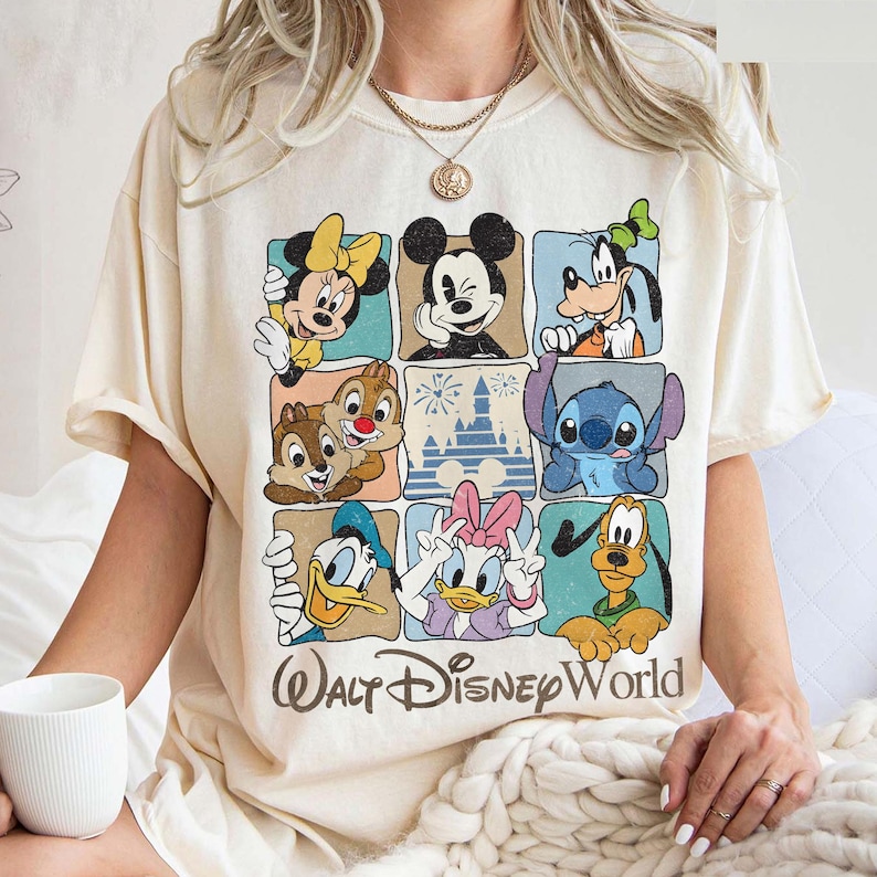 May include: Cream-colored t-shirt featuring a grid of Disney characters including Mickey Mouse, Minnie Mouse, Goofy, Donald Duck, Daisy Duck, Chip and Dale, Stitch, and Pluto. The words "Walt Disney World" are printed below the grid in a brown font.
