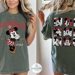 May include: Olive green t-shirt featuring a Minnie Mouse graphic. The front design includes the word "MINNIE" in red, the character, and the text "EST 1928". The back of the shirt displays nine Minnie Mouse portraits in red and white squares.