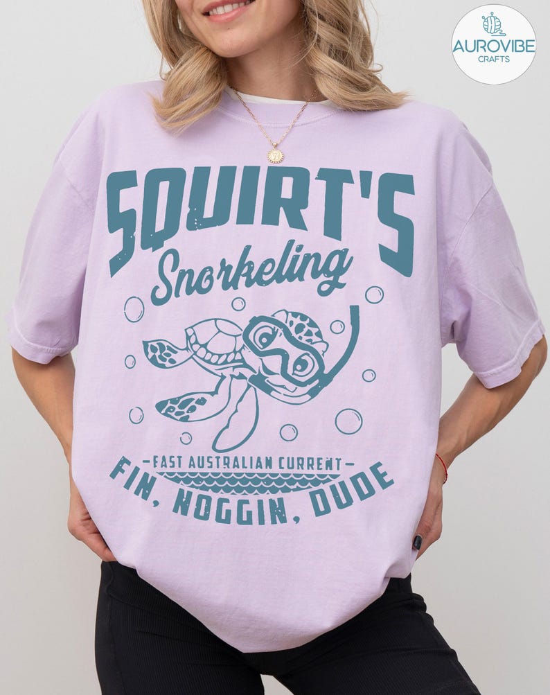 May include: A light purple t-shirt with the words "Squirt's Snorkeling" in teal. Below the text is a cartoon turtle wearing a snorkel. The shirt also has the text "Fin, Noggin, Dude" and "Fast Australian Current".
