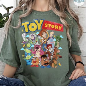 May include: Green t-shirt featuring the words "TOY STORY" in yellow and red, with a graphic of various characters from the animated film. The design includes Woody, Buzz Lightyear, and other beloved characters.