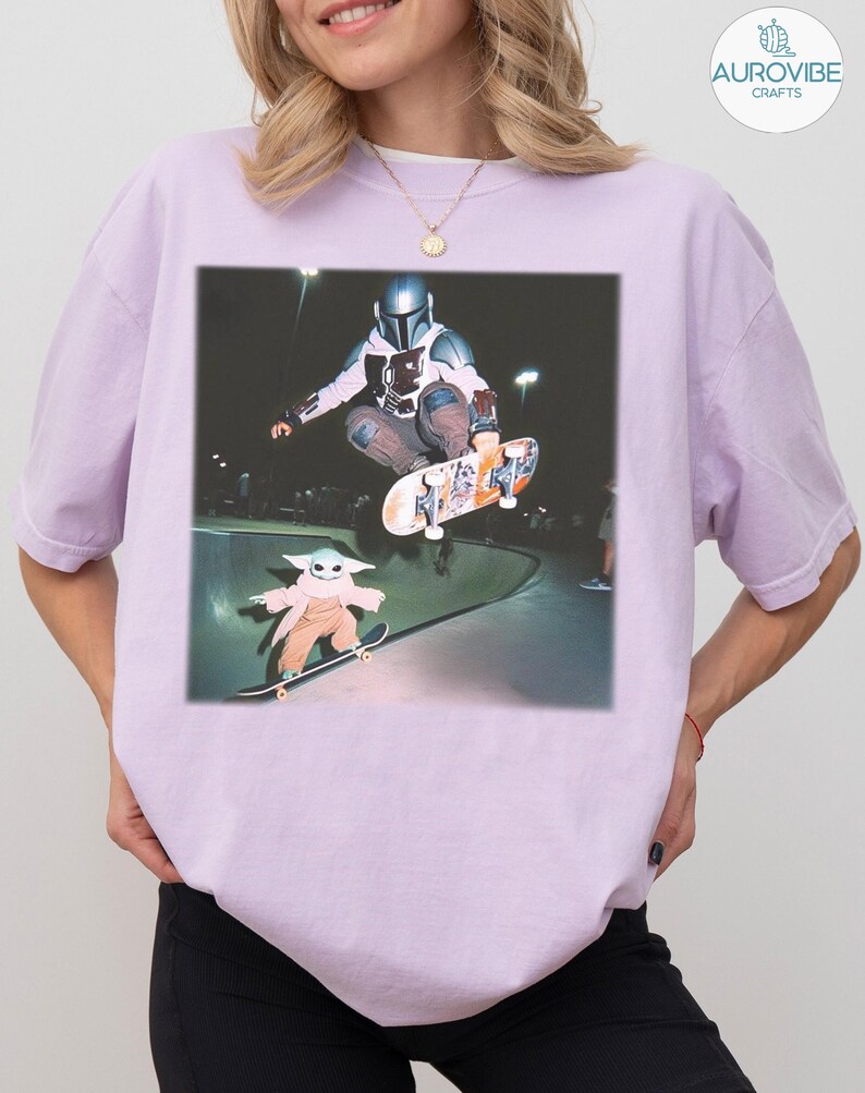Puede incluir: Una camiseta lila claro con un gr&aacute;fico de un skater con casco mandaloriano en el aire, con un personaje de Baby Yoda patinando debajo. La imagen est&aacute; ambientada en un skate park.