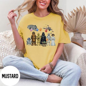 Peut inclure: T-shirt jaune moutarde avec un motif Star Wars. Le motif comprend des illustrations de personnages et de vaisseaux spatiaux de la franchise Star Wars. Le mot "MUSTARD" est imprim&eacute; en bas de l'image.