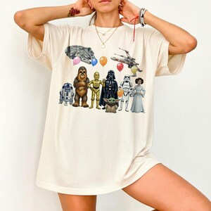 Peut inclure: T-shirt cr&egrave;me avec un graphisme color&eacute; de personnages de Star Wars, dont R2-D2, Chewbacca, C-3PO, Dark Vador, un Stormtrooper et la Princesse Leia. Le motif comprend &eacute;galement le Faucon Millenium, un X-wing et des ballons.