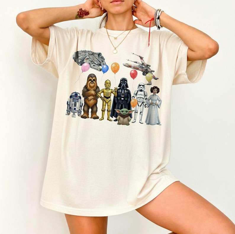 Peut inclure: T-shirt cr&egrave;me avec un graphisme color&eacute; de personnages de Star Wars, dont R2-D2, Chewbacca, C-3PO, Dark Vador, un Stormtrooper et la Princesse Leia. Le motif comprend &eacute;galement le Faucon Millenium, un X-wing et des ballons.