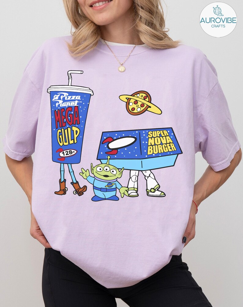 以下が含まれることがあります： トイ・ストーリーの漫画グラフィックが特徴の薄紫色のTシャツ。デザインには、メガガルフドリンク、ピザプラネットピザ、スーパーノヴァバーガーボックス、緑色のエイリアンキャラクターが含まれています。