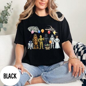 Peut inclure: T-shirt noir avec un motif Star Wars. Le motif comprend des illustrations de personnages tels que R2-D2, Chewbacca, C-3PO, Dark Vador, un Stormtrooper et la Princesse Leia, ainsi qu'un Faucon Millenium et un X-wing.