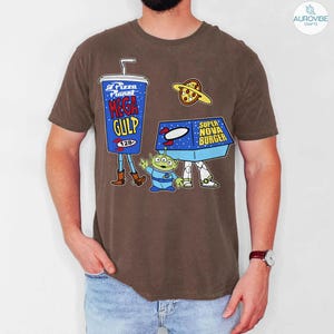 以下が含まれることがあります： 茶色のTシャツ。映画トイ・ストーリーの漫画のグラフィックが特徴です。デザインには、メガガルフドリンク、スーパーノヴァバーガーボックス、ピザプラネット、緑色のエイリアンキャラクターが含まれています。Tシャツはクルーネックと半袖です。