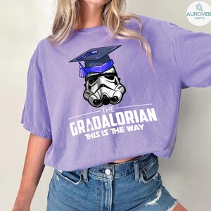Pu&ograve; includere: T-shirt lilla con un casco da Stormtrooper con cappello di laurea. Il testo "THE GRADALORIAN THIS IS THE WAY" &egrave; stampato in bianco. La maglietta &egrave; realizzata in materiale morbido.