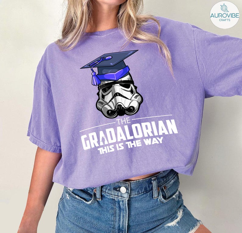 Pu&ograve; includere: T-shirt lilla con un casco da Stormtrooper con cappello di laurea. Il testo "THE GRADALORIAN THIS IS THE WAY" &egrave; stampato in bianco. La maglietta &egrave; realizzata in materiale morbido.