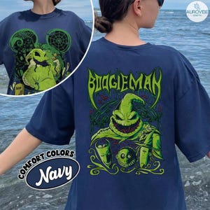 May include: A navy blue t-shirt featuring a large, vibrant green graphic of the Boogieman character with a wide, toothy grin, dice, and smaller character faces. The text BOOGIEMAN is printed in a stylised, dripping green font above the character.