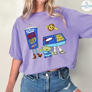 以下が含まれることがあります： 人気アニメ映画の漫画グラフィックが特徴のライラック色のTシャツ。デザインには、メガガルのカップ、ピザプラネット、スーパーノヴァバーガーボックス、緑色のエイリアンキャラクターが含まれています。このシャツは快適でカジュアルなスタイルです。