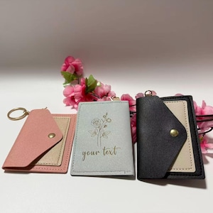 May include: Three small rectangular card holders with envelope-style flaps and gold-tone snap buttons. One is dusty pink, one is light gray with a gold floral line drawing and the text 'your text', and one is black with a beige center panel.