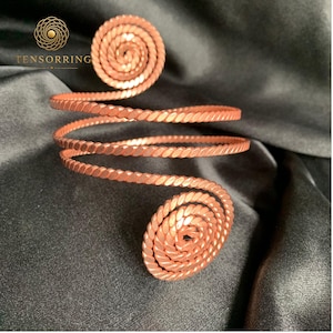 May include: A copper-colored metal arm cuff featuring a continuous spiral design with a twisted rope-like texture. The piece terminates in two circular coils at each end. The logo TENSORRING is visible in the upper left corner of the image.