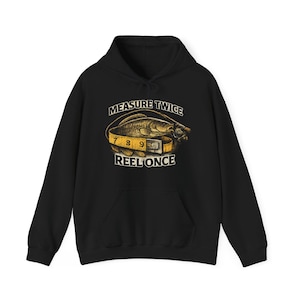 May include: Black hooded sweatshirt with a fishing-themed graphic. The graphic features a fish wrapped with a measuring tape, with the text "MEASURE TWICE REEL ONCE" in white. The sweatshirt has a front pocket and a drawstring hood.