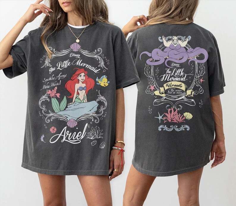 Może przedstawiać: Ciemnoszara koszulka z nadrukiem z przodu przedstawiającym Ariel z Małej Syrenki Disneya, z napisem "The Little Mermaid" i "Ariel". Tył koszulki przedstawia Urszulę oraz napisy "The Little Mermaid" i "Ursula".