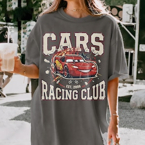 May include: Gray t-shirt featuring a graphic of the animated character Lightning McQueen from the movie Cars. The design includes the text "CARS RACING CLUB EST. 2006" in a vintage style.