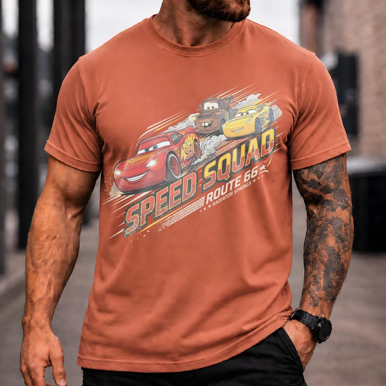 Op de afbeelding: Roestkleurig T-shirt met een afbeelding van de Cars-filmfiguren: Bliksem McQueen, Takel en een gele auto. De tekst "SPEED SQUAD ROUTE 66 RADIATOR SPRINGS" staat op de voorkant. Het shirt heeft korte mouwen.
