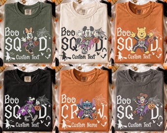 May include: Six crew neck t-shirts in olive, cream, orange, black, rust, and charcoal. Each features a graphic of a cartoon character in a skeleton costume, a spider web, bats, a witch on a broom, and the text Boo Squad or Boo Crew with Custom Text.