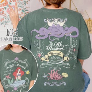 Może przedstawiać: Zielona koszulka w kolorze mchu z grafiką z Małej Syrenki Disneya. Projekt z tyłu zawiera Urszulę, tekst "The Little Mermaid" i "The ocean will be mine." Prz&oacute;d przedstawia Ariel, Florka i tekst "Spatele Agony Neue Moinch."