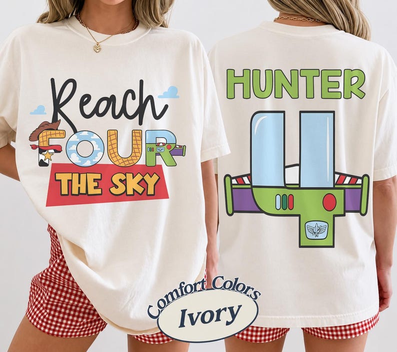 以下が含まれることがあります： 黒、青、赤、黄色の「Reach FOUR the SKY」の文字が入ったアイボリー色のTシャツ。背中には、緑、紫、青のグラフィックの上に緑色の「HUNTER」という名前がプリントされています。このシャツはComfort Colorsコレクションの一部です。
