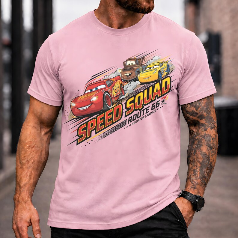Op de afbeelding: Een lichtroze t-shirt met de tekst "Speed Squad Route 66 Radiator Springs" en illustraties van drie cartoonauto's. De auto's zijn rood, bruin en geel, met een racethema.