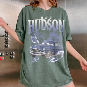 May include: A white ceramic mug with a black handle and the text "But First, Coffee" in a black, bold font. The mug is on a white surface.