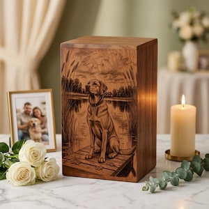 Puede incluir: Una urna funeraria rectangular de madera con una ilustración grabada con láser de un Labrador sentado en un muelle de madera junto a un lago, con juncos altos, nubes y hojas caídas en un estilo detallado de pirograbado.