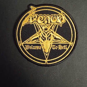 Peut inclure: Écusson noir et or brodé avec un pentagramme et une tête de bouc au centre. Le mot "Venom" est en haut et "Welcome To Hell" en bas, le tout en lettres dorées.