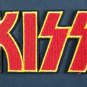 Peut inclure: Un écusson brodé rectangulaire affichant le mot KISS en lettres rouges stylisées et audacieuses. Les lettres présentent une bordure jaune vif et un fin contour noir, créant un design contrasté prêt à être appliqué sur des articles en tissu.