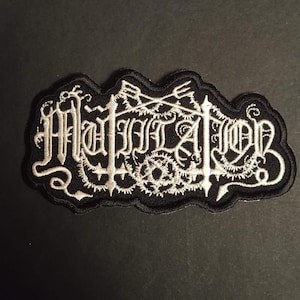 Peut inclure: Écusson brodé noir et blanc avec le mot "Mutation" en lettres gothiques. Le patch a une bordure noire et un motif décoratif autour du texte.