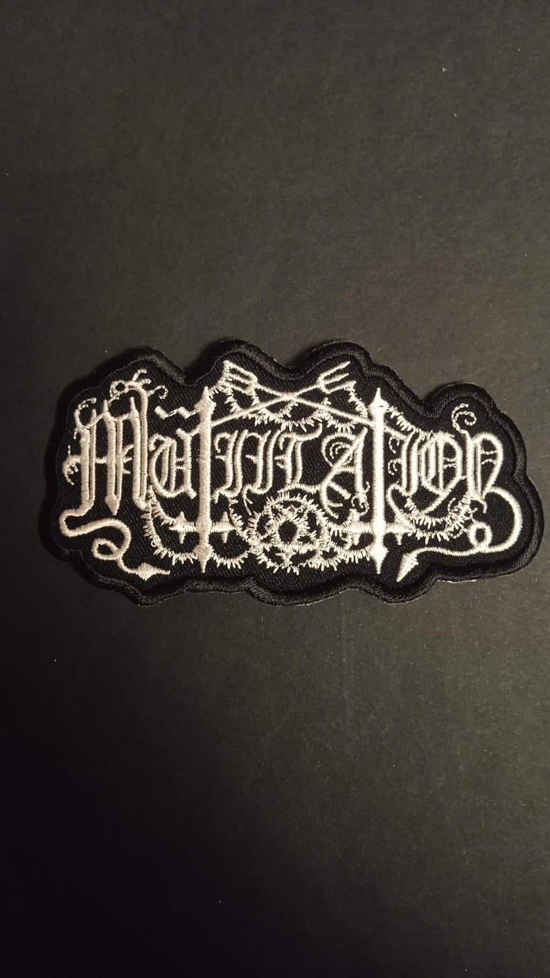K&ouml;nnte beinhalten: Schwarz-wei&szlig;er gestickter Aufn&auml;her mit dem Wort "Mutation" in gotischer Schrift. Der Aufn&auml;her hat einen schwarzen Rand und ein dekoratives Design um den Text.