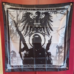 May include: Black and white flag with a central image of a silhouetted figure with raised arms and a halo, holding a weapon. An eagle and inverted crosses are above the figure. The text "SATANIC WARMASTER" and "BLACK METAL KOMMANDO / GAS CHAMBER" are printed.
