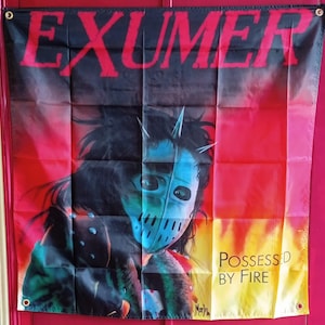 Könnte beinhalten: Ein rechteckiges Wandbanner aus Stoff mit dem roten Schriftzug EXUMER oben und dem schwarzen Text POSSESSED BY FIRE unten rechts. Die zentrale Grafik zeigt eine Figur mit einer blauen Hockeymaske vor einem roten und gelben Hintergrund.