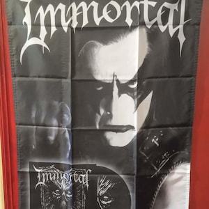 Könnte beinhalten: Schwarz-weiße Immortal-Bandflagge. Die Flagge zeigt den Namen der Band in einer gotischen Schrift oben. Die Flagge hat eine Collage von Bildern, darunter eine Nahaufnahme des Gesichts eines Bandmitglieds und Albumkunst. Der Text "Northern Chaos Gods" ist ebenfalls sichtbar.