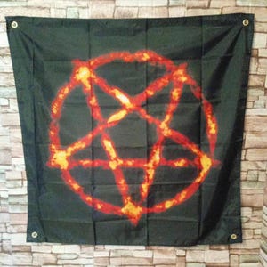 May include: A square black fabric wall hanging featuring a large, centered pentagram graphic. The pentagram is rendered in a fiery, textured pattern of orange, yellow, and red hues. The banner includes four metal grommets, one in each corner.