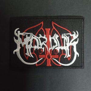 Peut inclure: Écusson rectangulaire noir avec texte et symboles brodés en blanc et rouge. Le motif présente des lettres stylisées et un symbole en forme de croix en rouge, sur fond noir. L'écusson est probablement destiné aux vêtements ou aux accessoires.