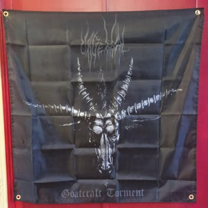 May include: Black flag featuring a white illustration of a goat's head with large horns and the text "Goatcraft Torment." The flag has metal grommets in each corner for hanging. The top of the flag has the text "Vile Lye Rites."