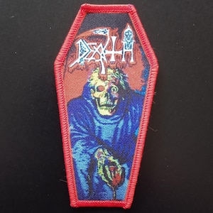 Op de afbeelding: Een doodskistvormige geborduurde patch met een rode gestikte rand. Het ontwerp toont een afbeelding van een skeletfiguur in een blauw gewaad met het woord DEATH in witte gestileerde letters bovenaan tegen een donkere achtergrond.